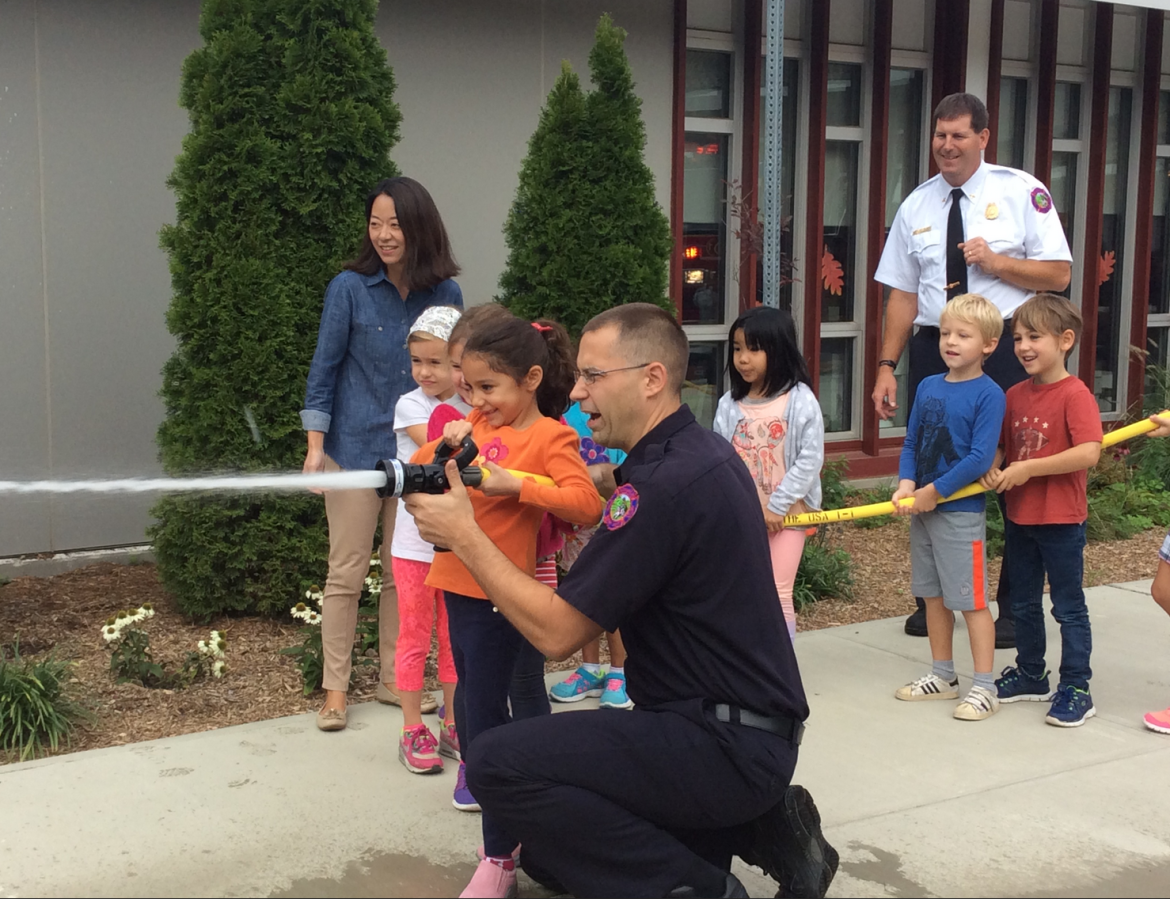 Pictured: First grader, Gabriela Estela, gets a lesson in fire safety from Sound Beach Fire Department’s Firefighter George Lattanzi. Her teacher, Mrs. You (far left), and Deputy Fire Marshal, Chris Moynahan (far right), look on while classmates Tess Keegan, Patrice Reyes, Sylvester Vagner and Niclas Nobile assist by holding the hose. 