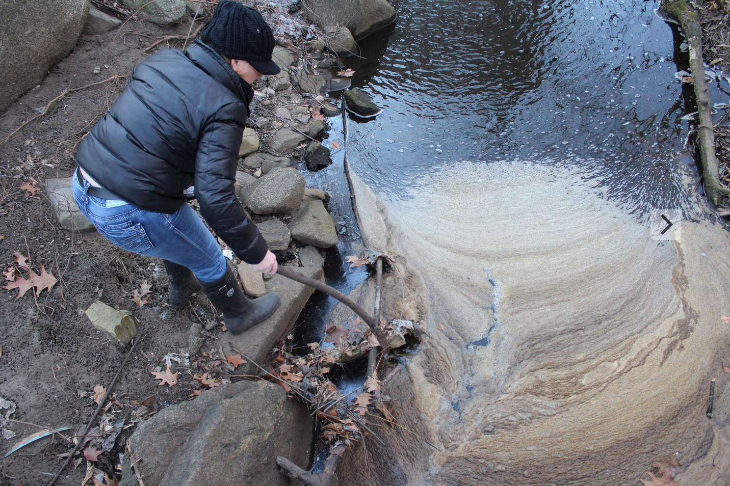 Dawn Fortunato drags a stick through brown crud on the brook behind Holy Hill. 