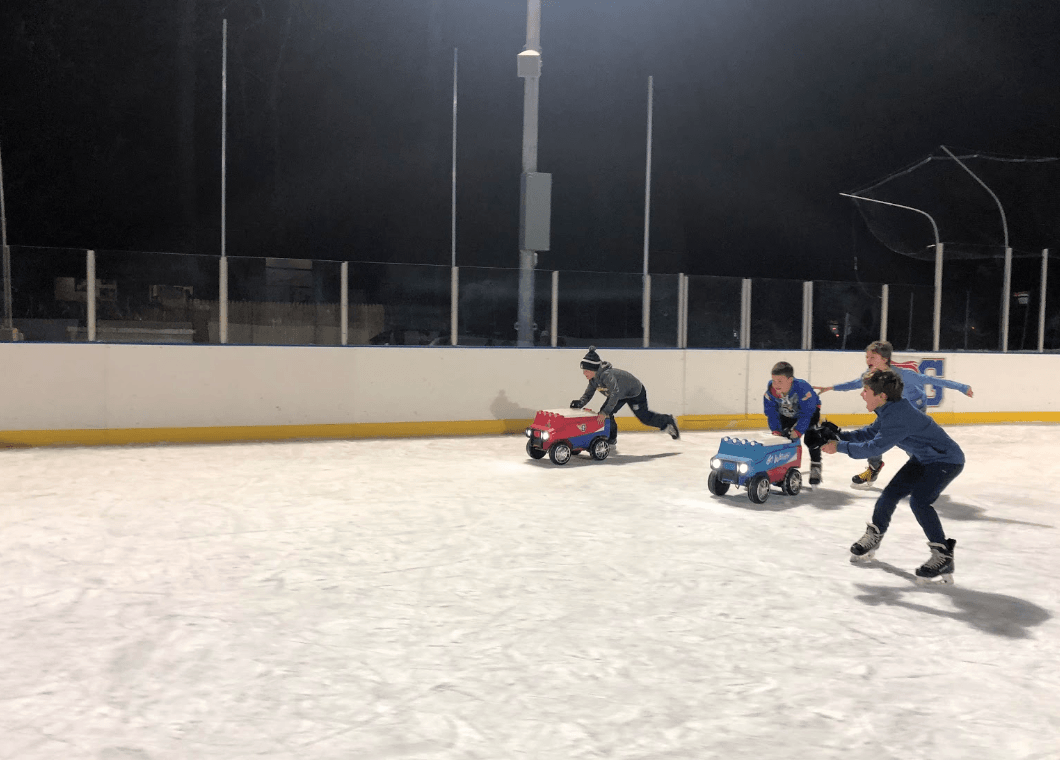 Nick and James push their zambonis around the rink while friends cheer them on